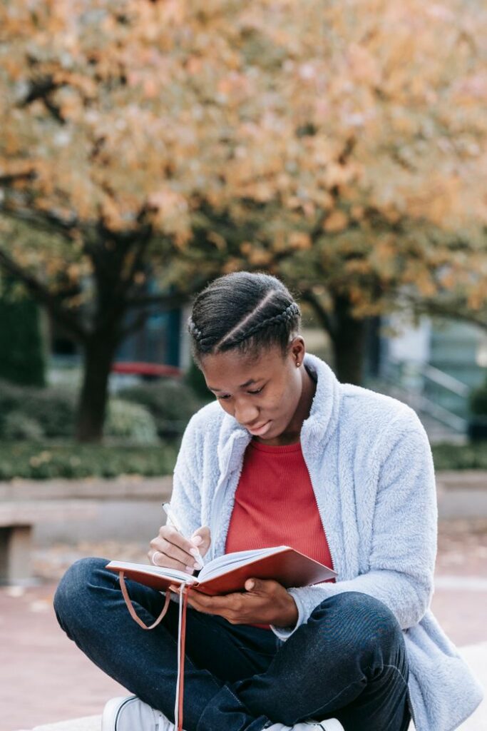 pexels photo 5965579 Young concentrated African American female student watching agenda while sitting with crossed legs in town