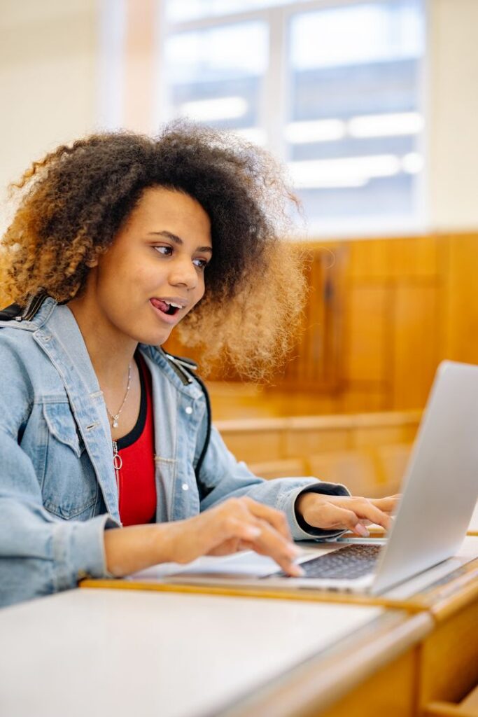 pexels photo 8197550 Young woman with curly hair studying on laptop in a bright classroom setting.
